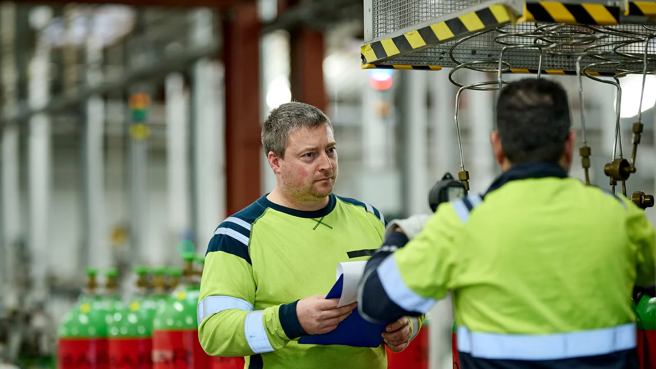 Glade medarbejdere på fabrik mellem flasker snakker om arbejdsplads. Sikkert arbejde i gas industri. 